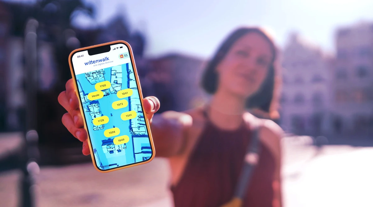 Eine junge Frau hält ein Smartphone in die Kamera. Auf dem Smartphone ist der Startbildschirm der wittenwalk App geöffnet.